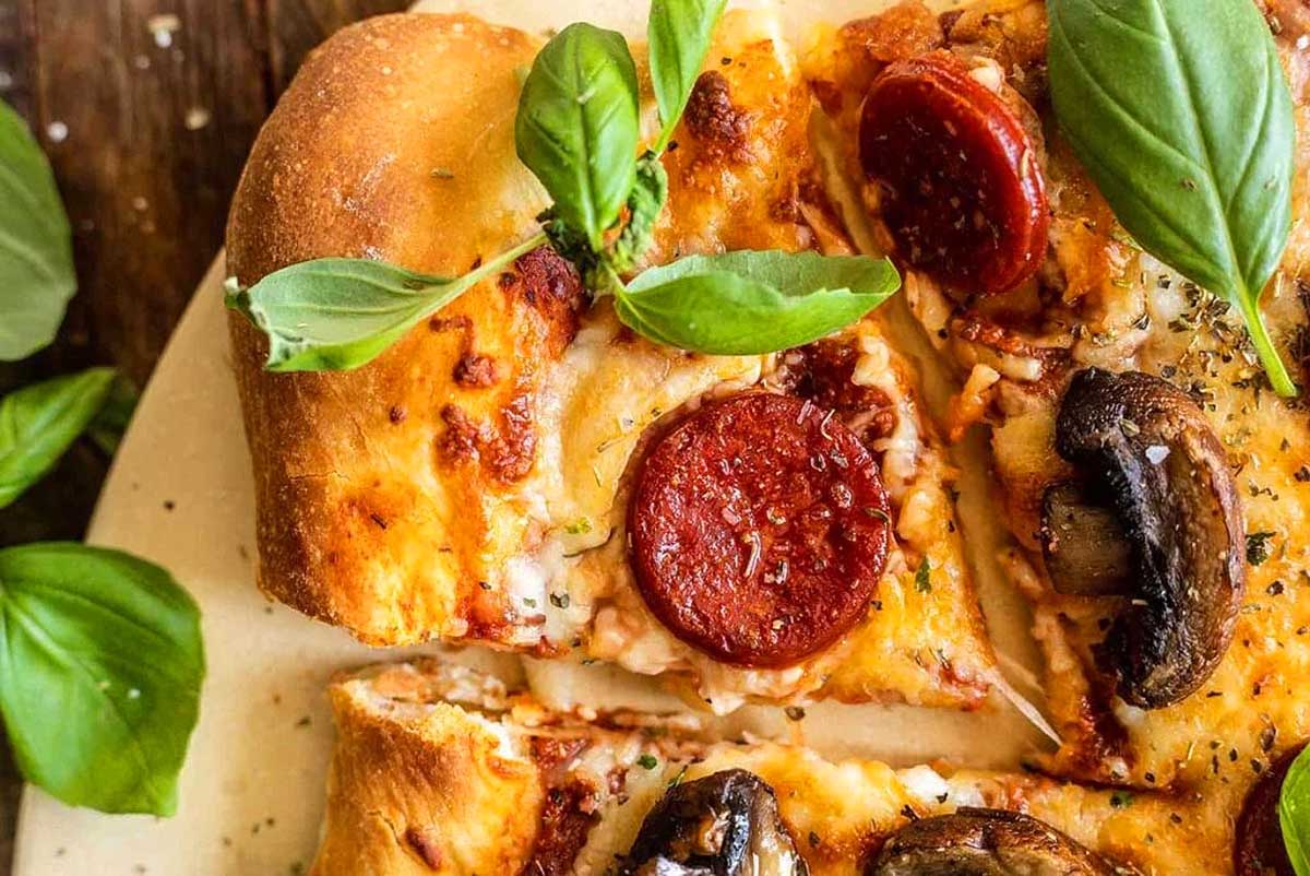 A slice of pizza with pepperoni, mushrooms and basil leaves.