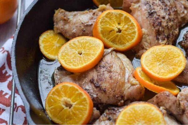 Chicken with orange slices in a skillet.