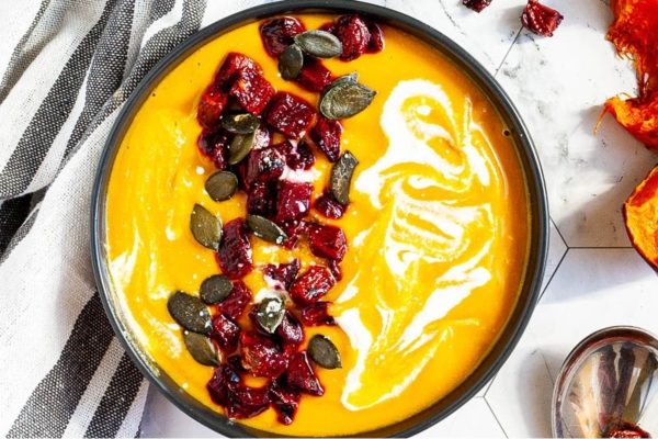A bowl of creamy pumpkin soup with cranberries and seeds.