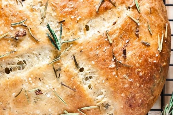 A loaf of bread with rosemary sprigs on a cooling rack.