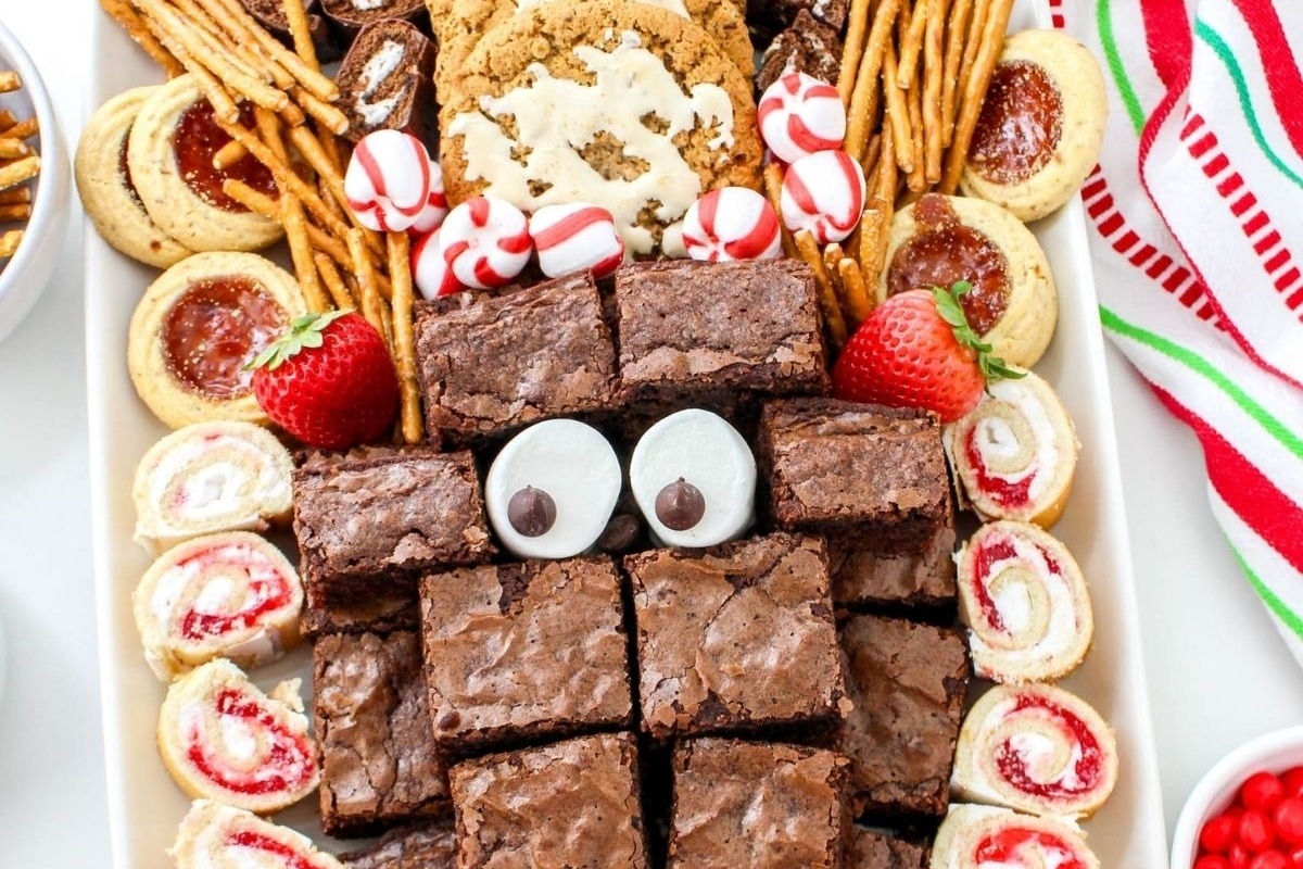A festive charcuterie board filled with an assortment of Christmas desserts including brownies, cookies, and candies.