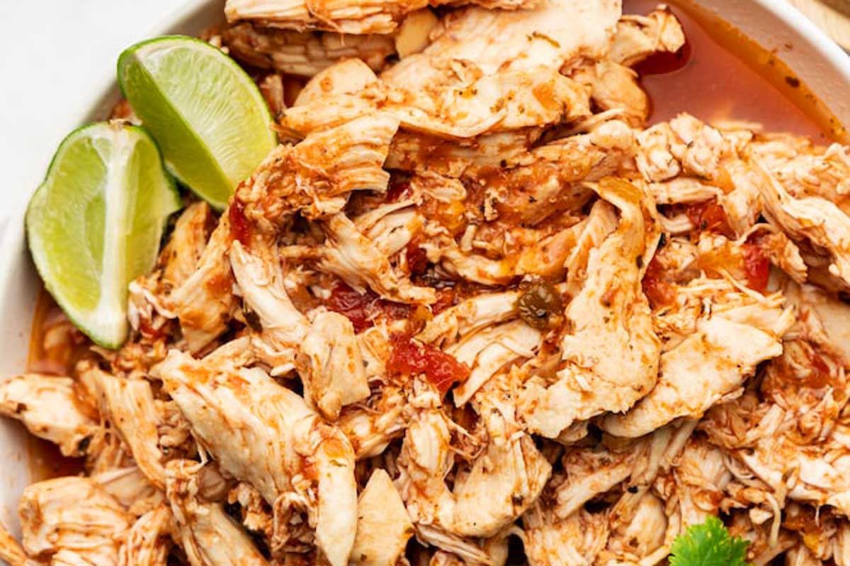 Shredded chicken in a white bowl with lime wedges.