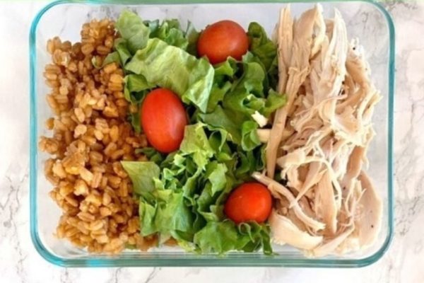 A glass container filled with chicken, rice, lettuce and tomatoes.
