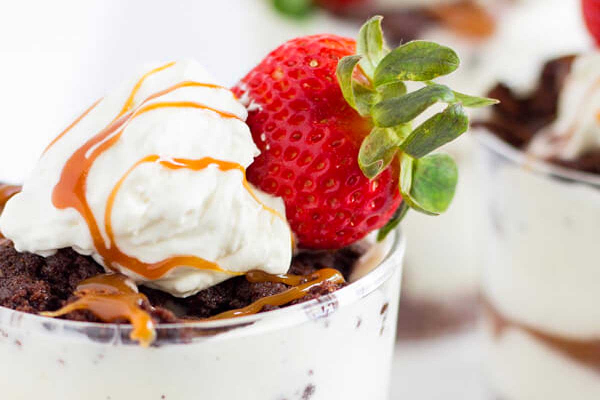 A chocolate dessert in a glass cup with strawberries and whipped cream.