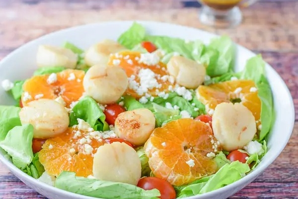 A bowl of salad with scallops, tomatoes and lettuce.