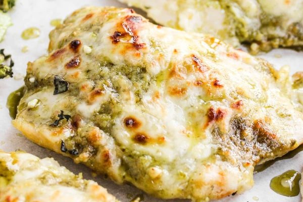 Chicken breasts with pesto and broccoli on a baking sheet.