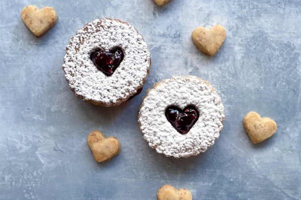 Two cookies with jam and powdered sugar on a blue background.