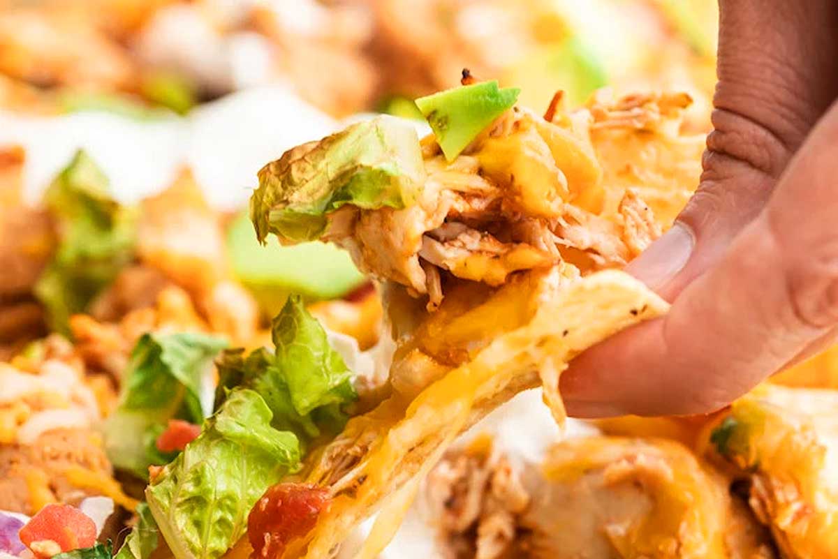 A person grabbing a piece of chicken nachos.