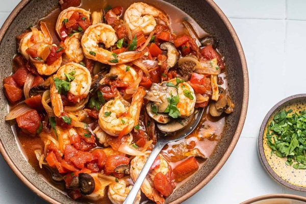 A bowl of shrimp stew with tomatoes and mushrooms.