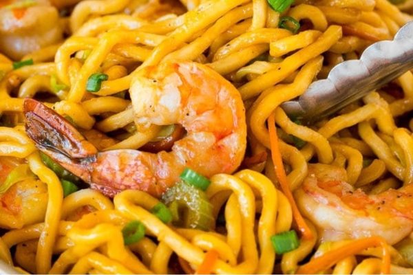 An Asian seafood recipe featuring a bowl of noodles with shrimp and vegetables.
