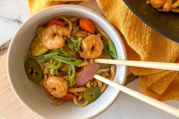 An Asian-inspired bowl of noodles with seafood, vegetables, and chopsticks. This delicious recipe showcases the perfect combination of flavors from fresh shrimp and an assortment of vibrant vegetables. Whether you're a