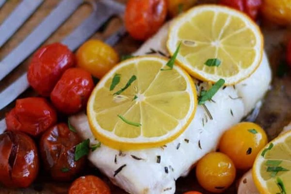 Fish fillets with lemon and tomatoes on a cutting board.