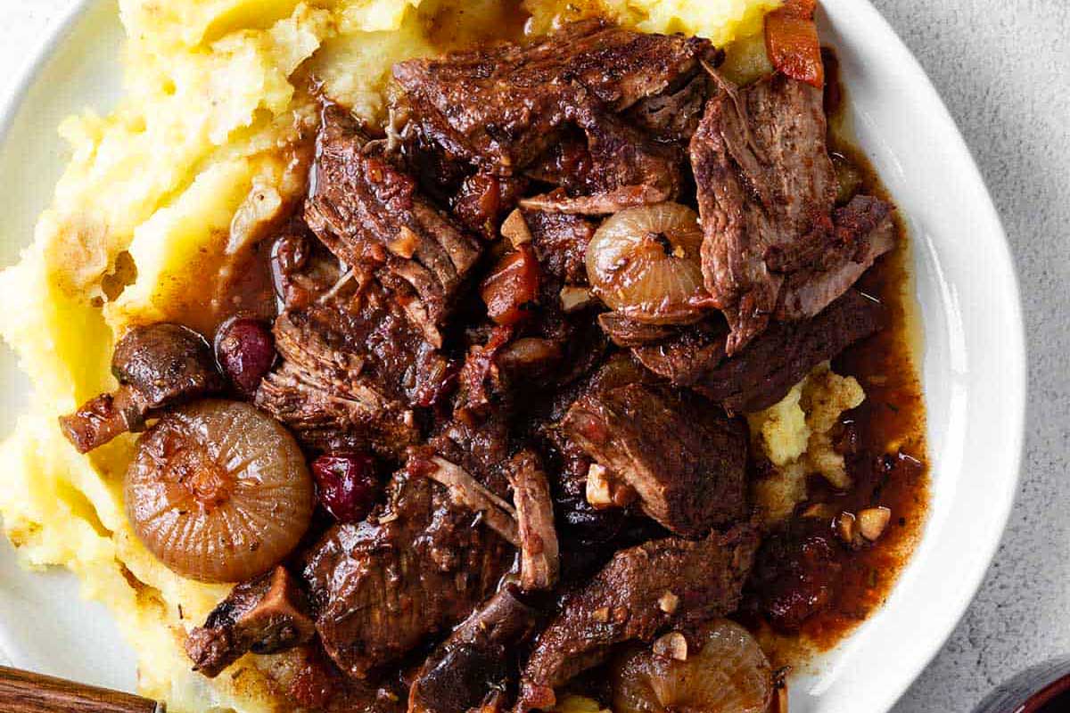 A white plate with beef and mashed potatoes.