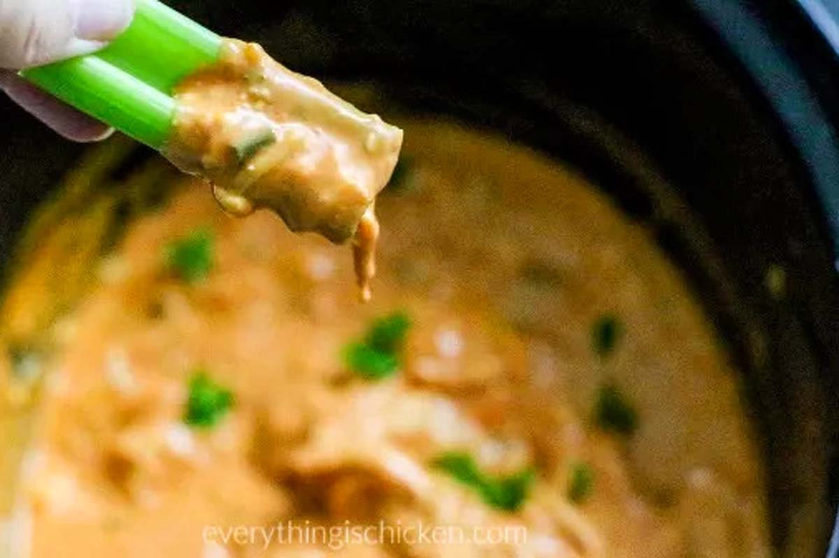 A person is preparing a slow cooker dip recipe by dipping a spoon into a crock pot.