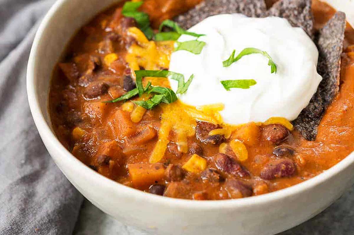 A delicious bowl of sweet potato chili topped with sour cream and served with tortilla chips. This hearty meal is packed with flavor and can be easily prepared in a slow cooker.