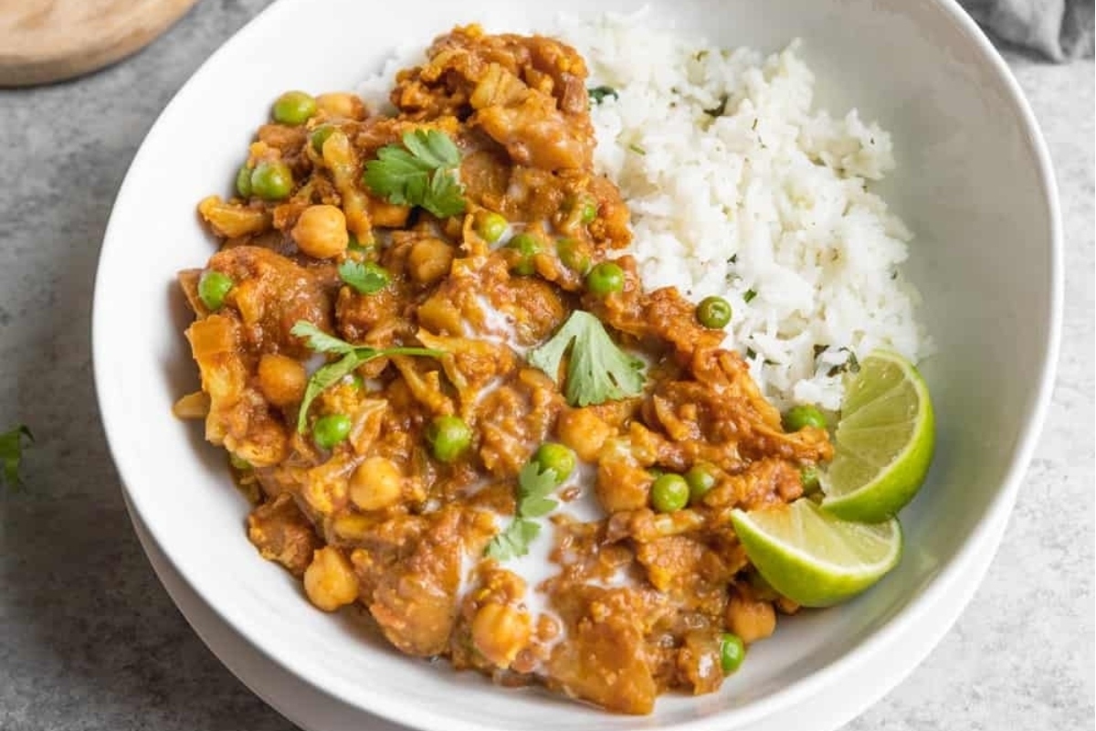 Chickpea curry in a bowl with rice and lime wedges.
