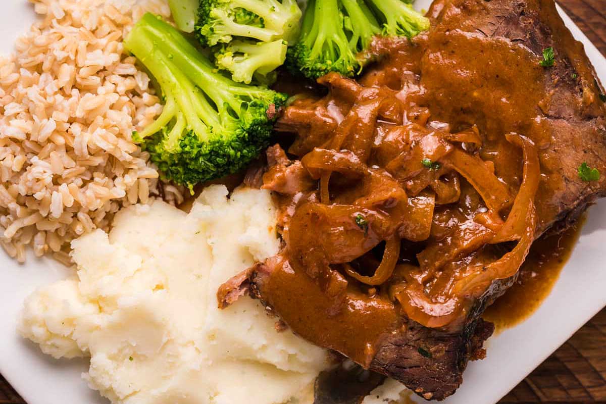 A plate with meat, mashed potatoes, broccoli and gravy.