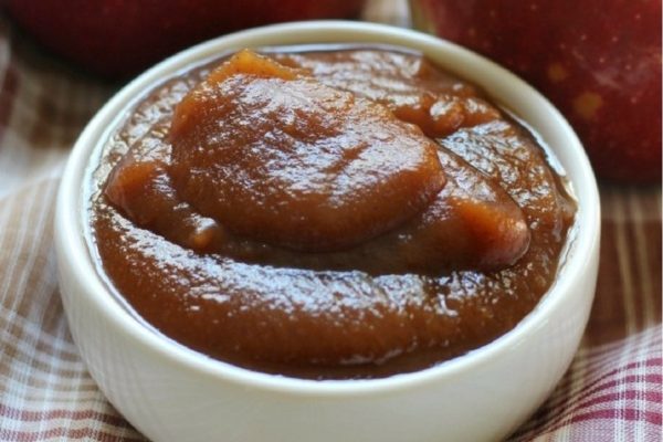 Applesauce in a white bowl with apples next to it.