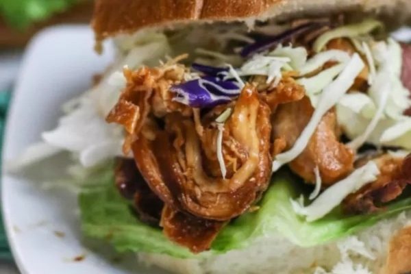 A bbq pulled pork sandwich with coleslaw on a white plate.