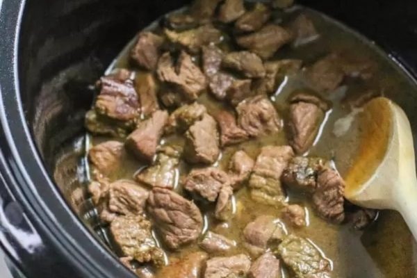 Beef stew in a slow cooker with a wooden spoon.