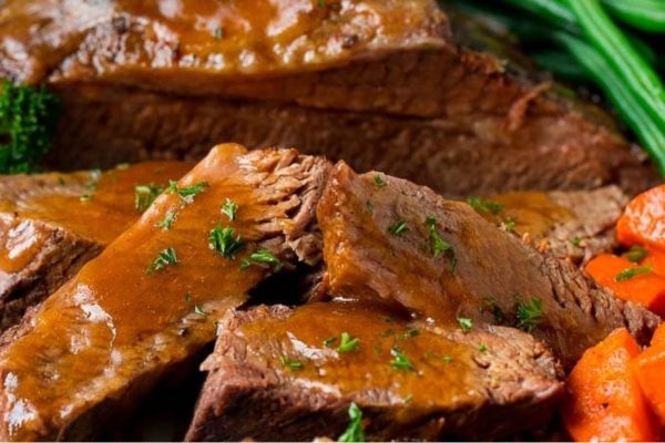 A plate of beef, carrots and gravy on a white plate.