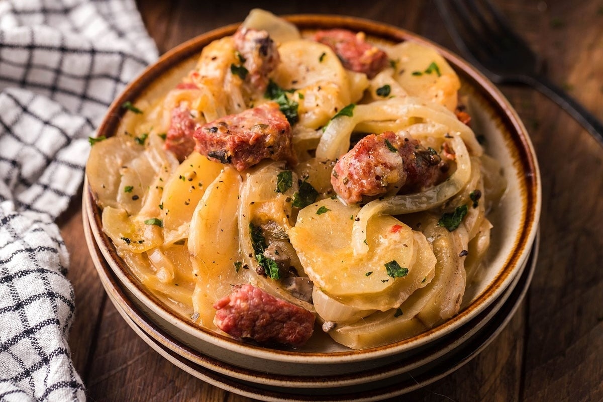 A bowl of sausage and onion soup on a wooden table.