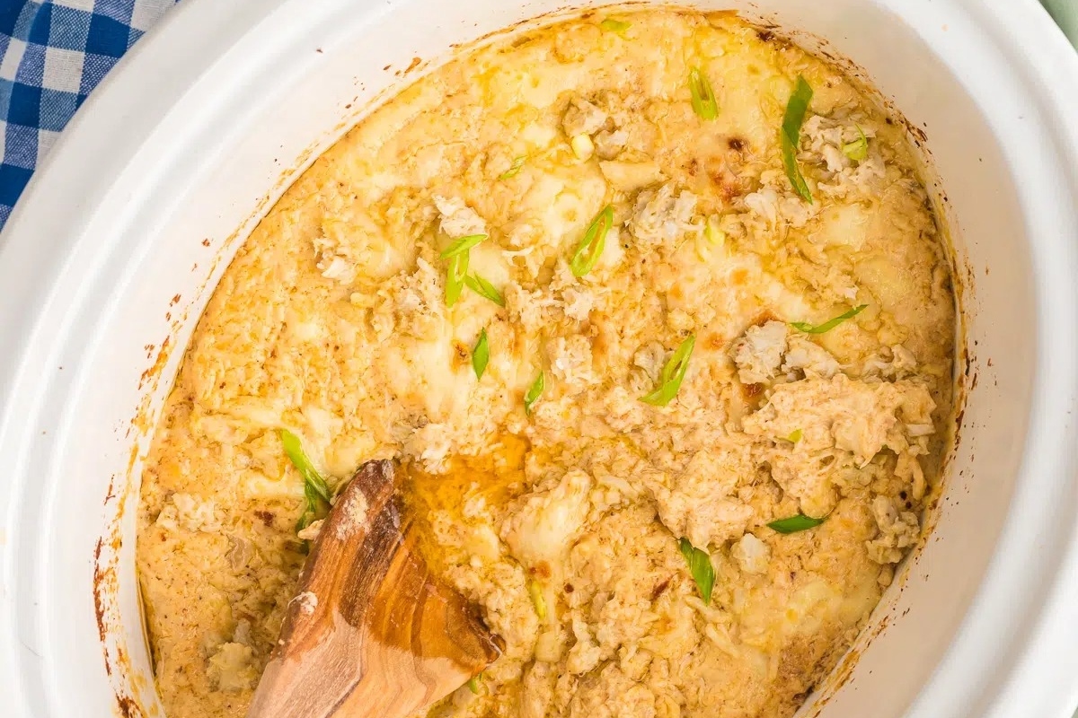 A slow cooker filled with delicious dips, accompanied by a wooden spoon for easy serving.