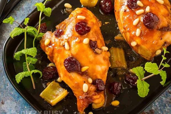Chicken breasts with cranberries and pine nuts on a black plate.
