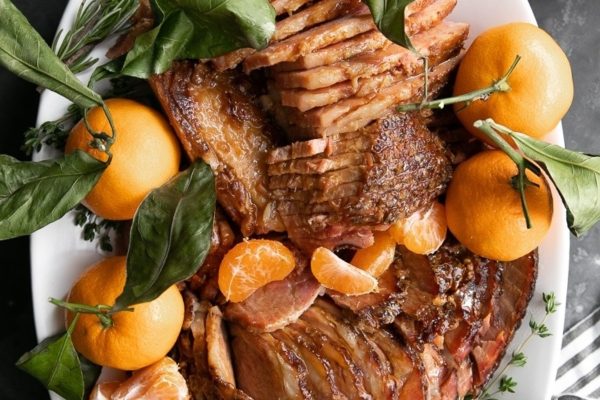 Roasted ham with oranges and herbs on a white plate.