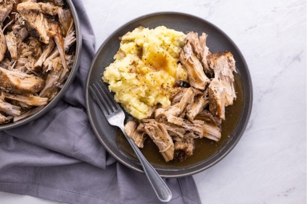 A plate of pulled pork with mashed potatoes and gravy.