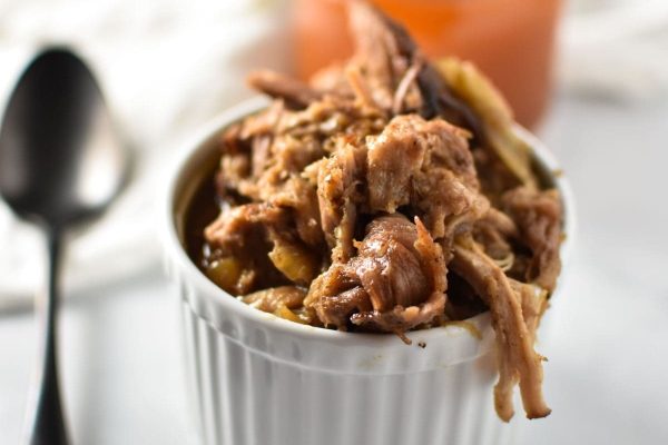 Pulled pork in a white bowl with a spoon.