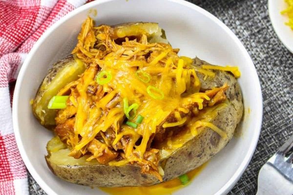 Cheesy baked potatoes in a white bowl with a fork.