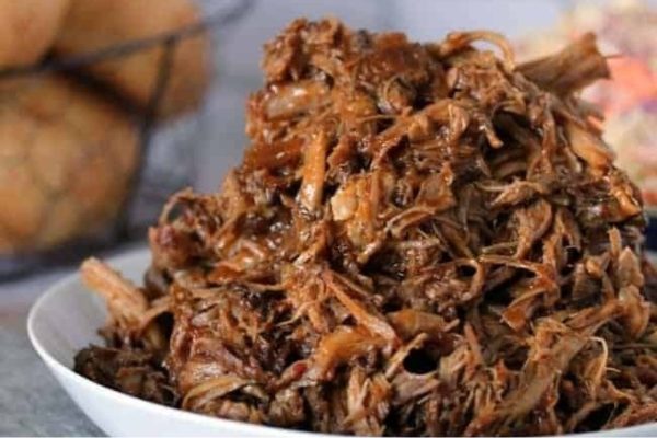 Slow cooker pulled pork in a white bowl.