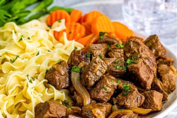 Beef stroganoff in a white bowl with carrots and noodles.