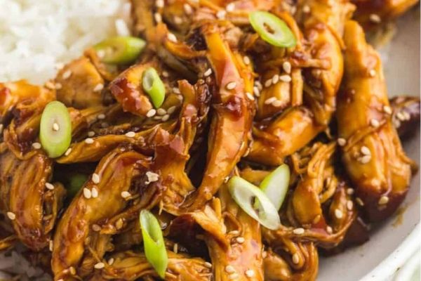 A bowl of asian chicken with rice and sesame seeds.