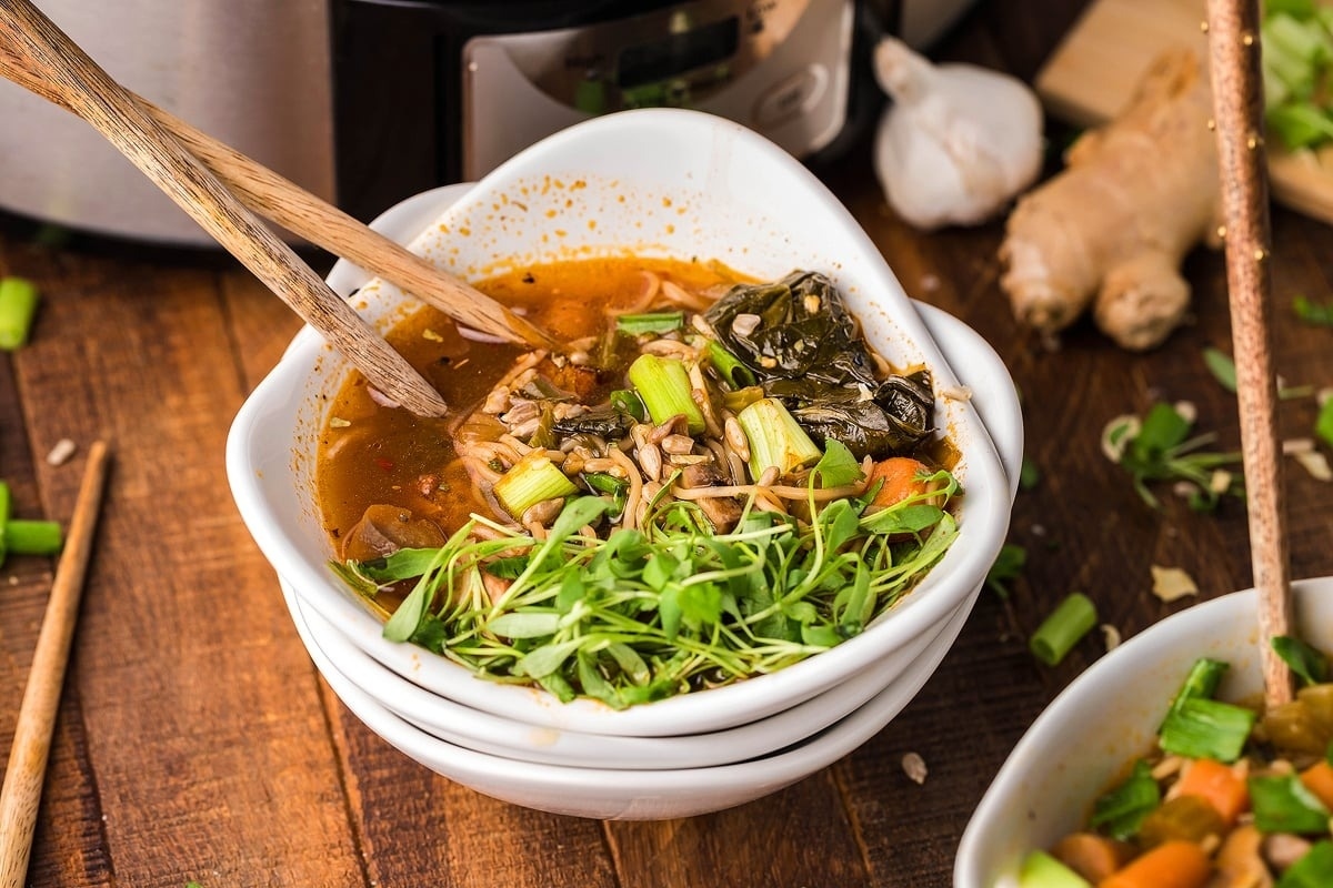 A bowl of soup with chopsticks in front of an instant pot.