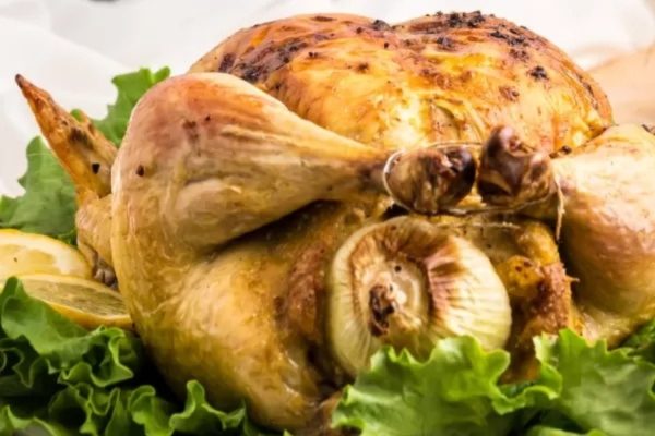 A roasted chicken on a plate with lettuce and lemons.