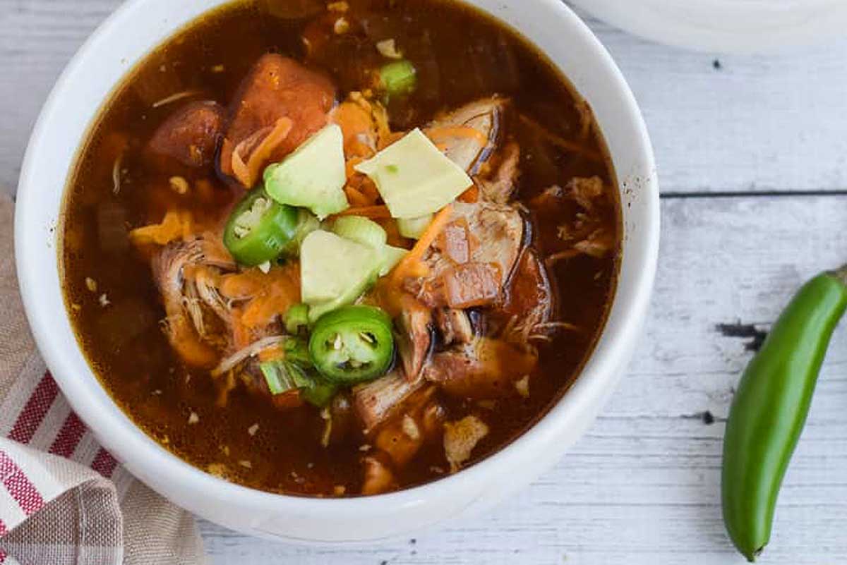 A bowl of mexican chicken soup on a wooden table.