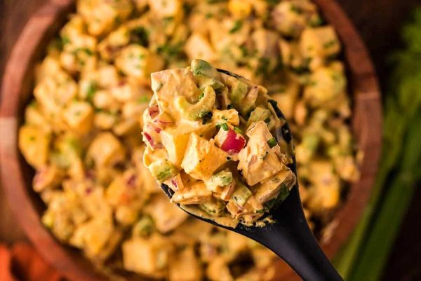 A spoon full of potato salad on a wooden table.