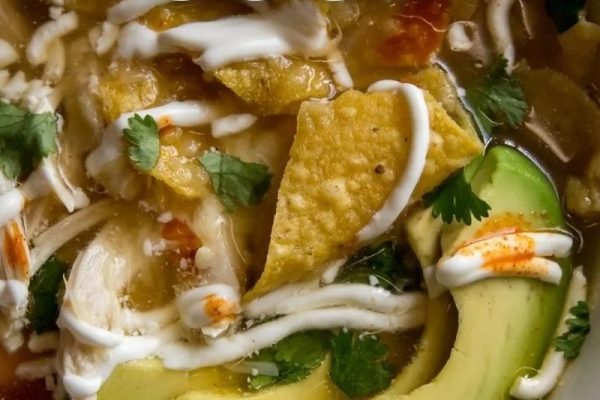 A bowl of chicken enchilada soup with avocado and sour cream.