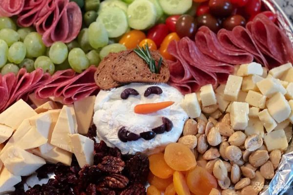 A Christmas-themed charcuterie board featuring a variety of cheeses and fruits, beautifully arranged with a festive snowman centerpiece.