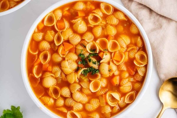 A bowl of pasta soup with carrots and parsley.