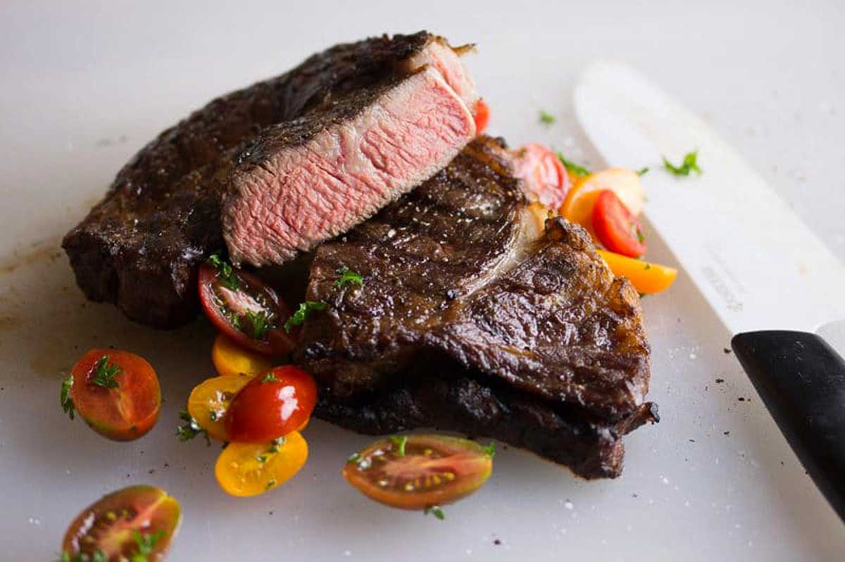 Steak on a cutting board with tomatoes and a knife.