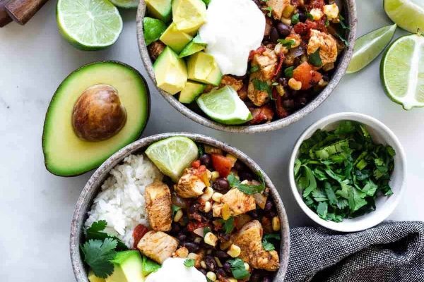 Two bowls of mexican chicken and rice with avocado and sour cream.
