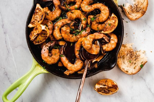 Grilled shrimp in a skillet with lemon slices.