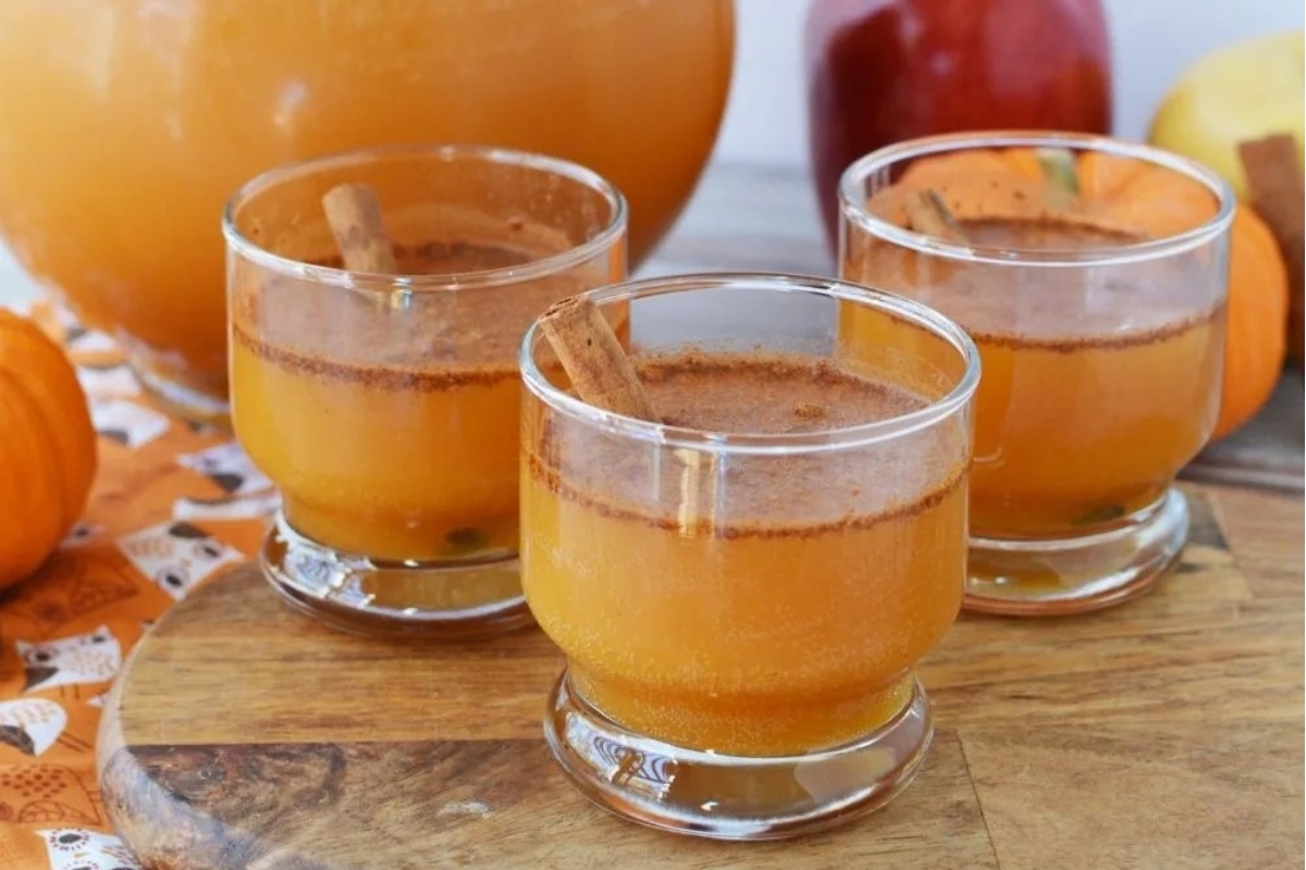 Three glasses of pumpkin juice with cinnamon sticks on a cutting board.