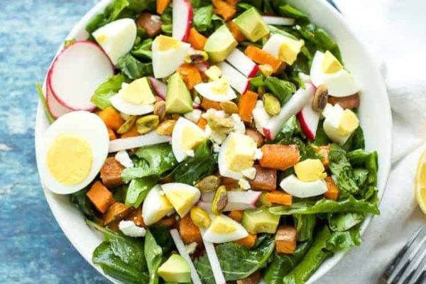A colorful bowl of spinach salad with eggs and radishes.