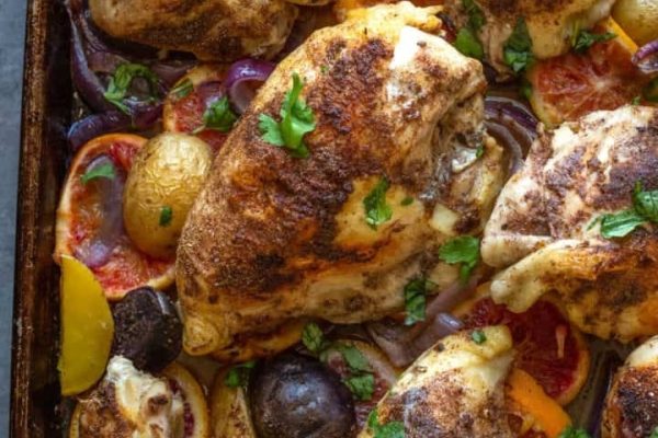 Roasted chicken with vegetables and herbs on a baking sheet.