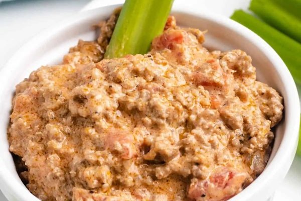 A bowl of sausage dip with celery and celery sticks.