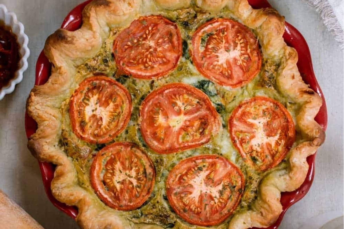 A country-style tomato and spinach quiche on a red plate.
